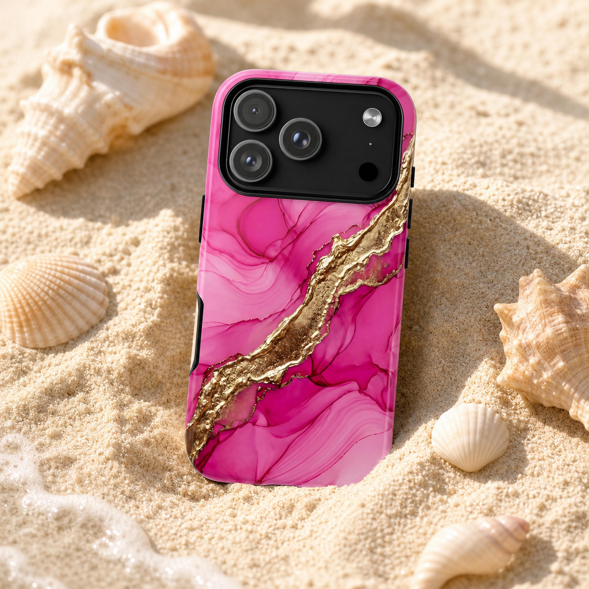 A pink marble-patterned phone case with a metallic gold vein design, shown on a smartphone lying on sandy beach ground surrounded by seashells.